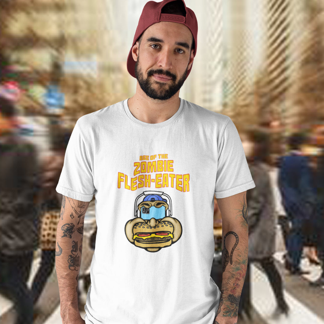 A man in a blurred crowded street wearing a white t-shirt with a graphic on the front. The graphic features the text 'AGE OF THE ZOMBIE FLESH-EATER' in yellow, above a cartoon zombie head wearing headphones and biting a burger.