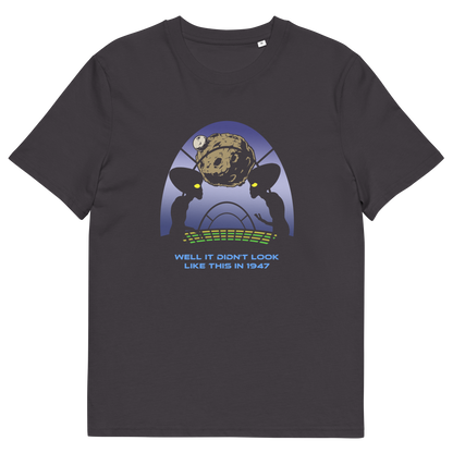 A dark charcoal gray crewneck t-shirt featuring a retro sci-fi graphic of two alien figures with large black eyes looking at a brown planet, with the text 'WELL IT DIDN'T LOOK LIKE THIS IN 1947' printed below.