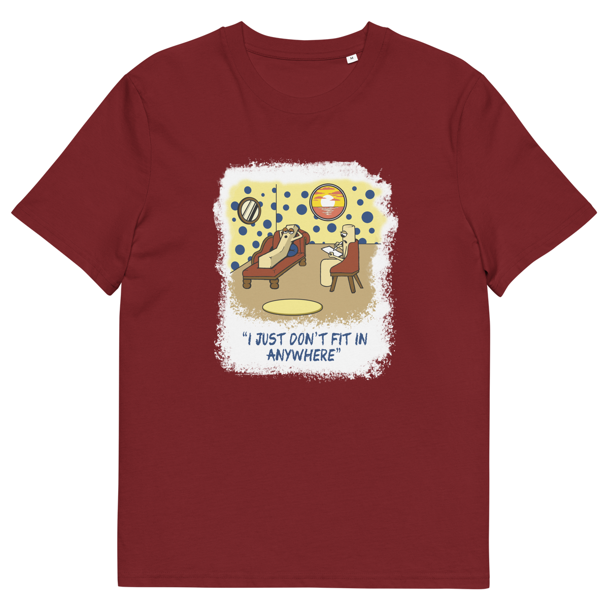 A burgundy short-sleeve crewneck t-shirt with a central graphic print. The graphic features a cartoon illustration of a person sitting on a lounge chair in a theorists room , with a white distressed border and the text 'I JUST DON'T FIT IN ANYWHERE' below.