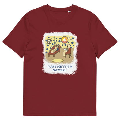 A burgundy short-sleeve crewneck t-shirt with a central graphic print. The graphic features a cartoon illustration of a person sitting on a lounge chair in a theorists room , with a white distressed border and the text 'I JUST DON'T FIT IN ANYWHERE' below.