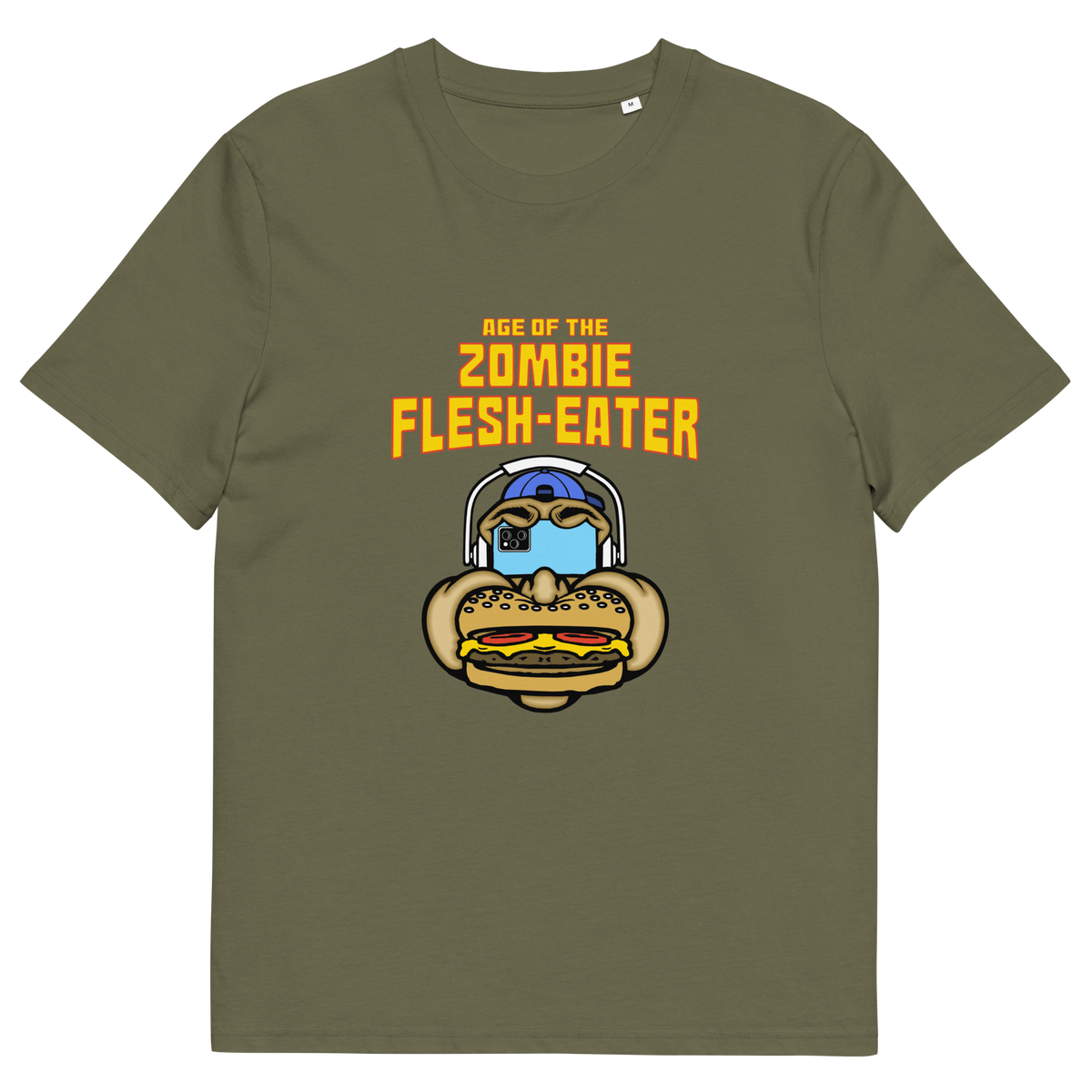 Khaki t-shirt with a graphic on the front. The graphic features the text 'AGE OF THE ZOMBIE FLESH-EATER' in yellow, above a cartoon zombie head wearing headphones and biting a burger.