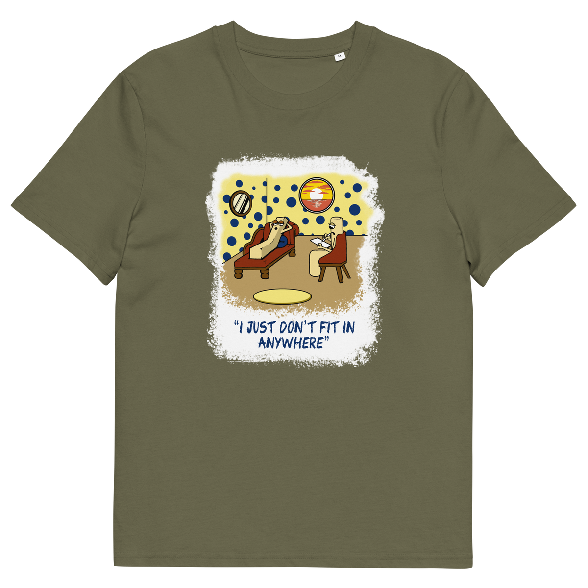 An khaki green short-sleeve t-shirt with a central graphic print. The graphic features a cartoon illustration of a person sitting on a lounge chair in a theorists room , with a white distressed border and the text 'I JUST DON'T FIT IN ANYWHERE' below.
