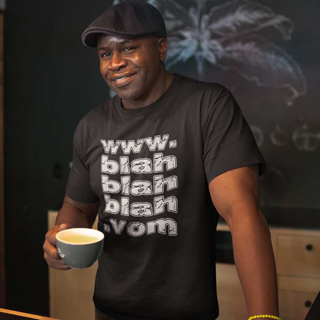 A man in a cap holding a cup and wearing a black t-shirt with "www.blahblahblah.vom" text design.