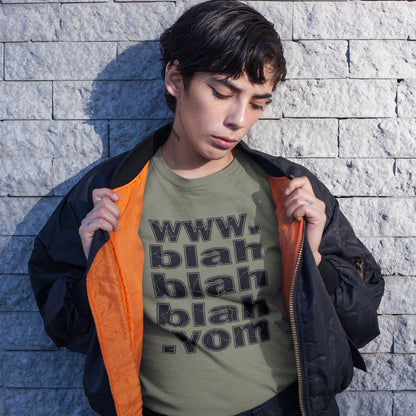 A woman standing against a brick wall, holding her jacket open, wearing a khaki green t-shirt with "www.blahblahblah.vom" text design.